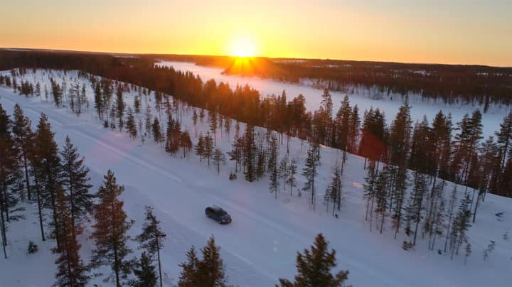 Bil på vintervei i skogen med solnedgang